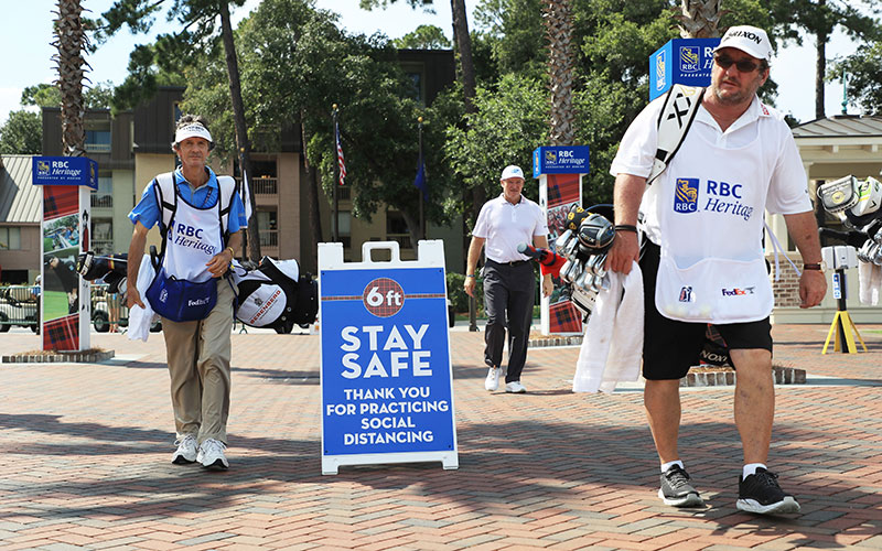 Caddies walk past signage promoting social distancing as a COVID-19 precaution during the second round of the RBC Heritage on June 19, 2020 at Harbour Town Golf Links in Hilton Head Island, South Carolina. (Photo by Streeter Lecka/Getty Images)